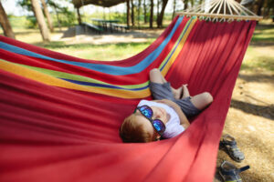 Cheerful little boy with sunglasses lying on hammock in a pine forest