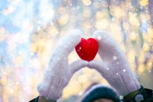 hands in white knitted mittens with a red heart on a snow background with bokeh. 